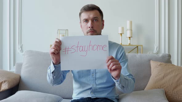 Man Sitting on a Sofa Warns of Coronavirus Disease Holds a Placard Stay at Home