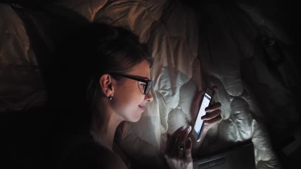 Teenage Girl on Touch Screen Smart Laptop and Headphones on Bed, Student in Dark Room with Mobile