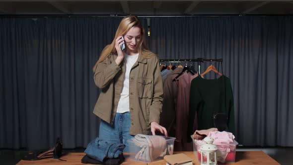 Young Woman Seller Talks on Phone and Works in Second Hand Clothes Shop