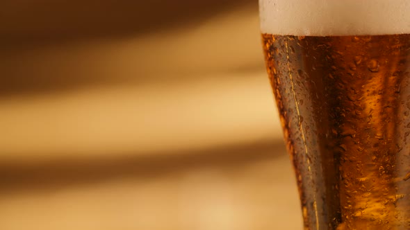 Closeup of Rotating Fresh Beer with Abstract Golden Background and Drops on Glass