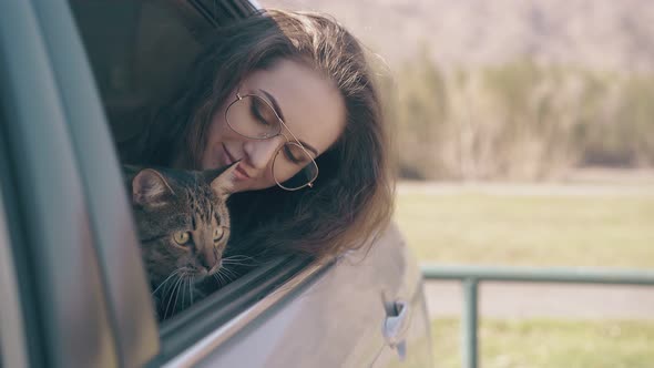 Happy Girl with Cute Cat Sits in Auto Against Meadow