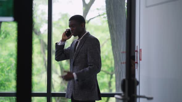 Nervous Stressed African American Young Man Arguing on Phone in Office with People Passing at Front