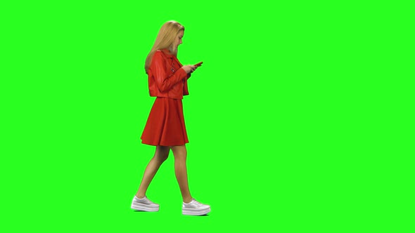 Blonde Girl Is Calmly Walking and Reading Text Message on Her Mobile Phone at Green Screen. Chroma