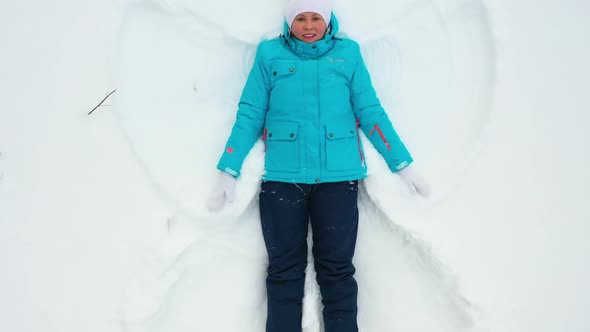 A Girl Makes a Figure of a Snow Angel in a Clearing in the Forest
