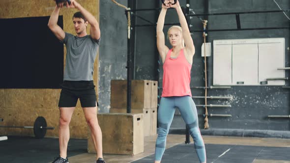 Girl and Guy in Sports Outfit Squatting with Kettlebells During Crossfit Training in Gym