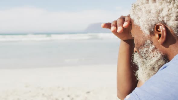 Senior african american man sitting and looking away on sunny beach