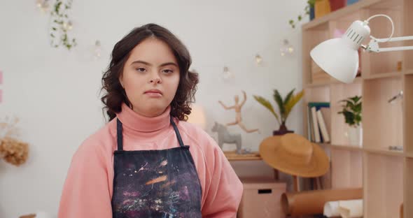 Portrait of Cute Pretty Girl with Down Syndromee Wearing in Artists Apron and Looking To Camera