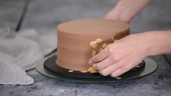 Female Pastry Chef Prepares a Cake and Decorates It with Almond Flakes.