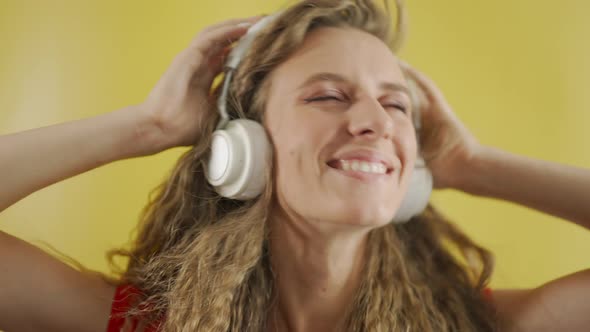 A Young Girl in Headphones is Listening to Music and Amusingly Dancing on a Yellow Background