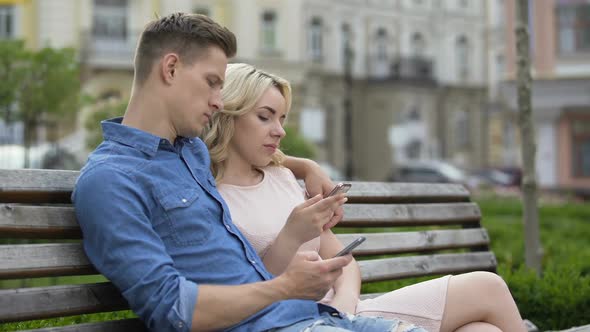 Boyfriend and Girlfriend Sitting on Bench, Engrossed in Phones, Networking