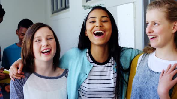 Smiling schoolgirls standing with arms around in corridor