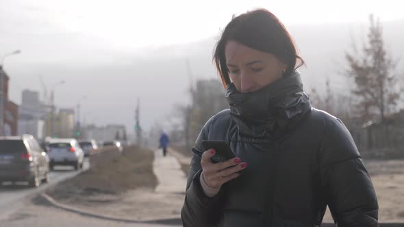 An Attractive Girl Uses Her Phone in the City Amid the Busy Traffic.