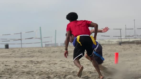 A group of guys playing flag football on the beach.