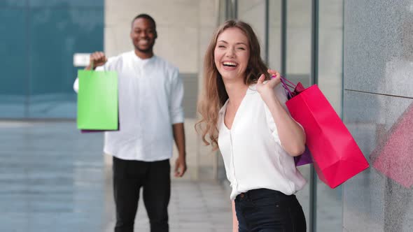 Caucasian Young Millennial Girl Woman Stands Near Blurred African American Guy Man Hold Shopping