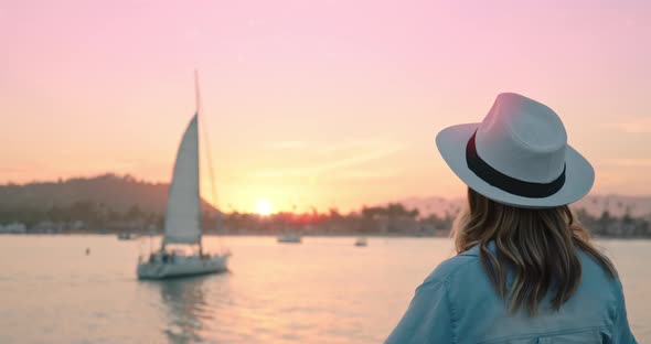 Elegant Lady Enjoying Scenic Pink and Gold Sunset While Sailboat Enters Harbor