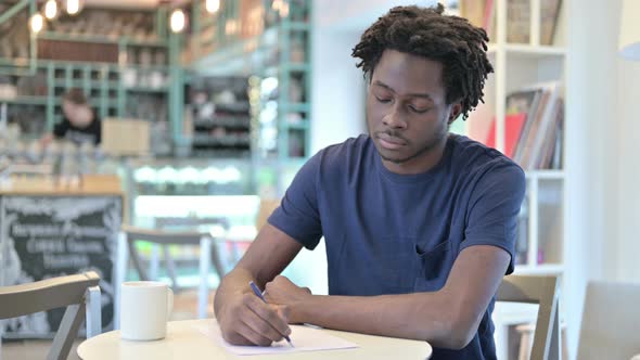 Thoughtful African Man Doing Paperwork in Cafe