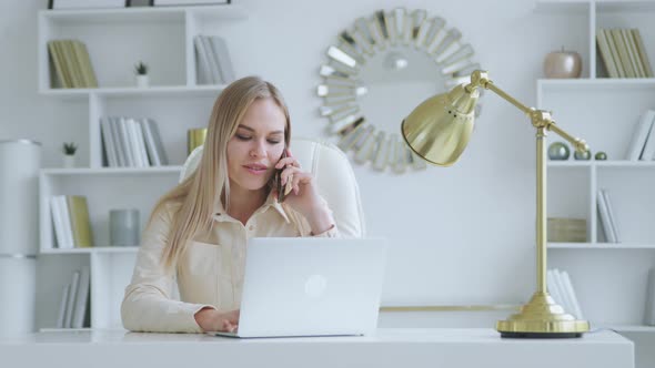 Young businesswoman with laptop talking on smartphone at home
