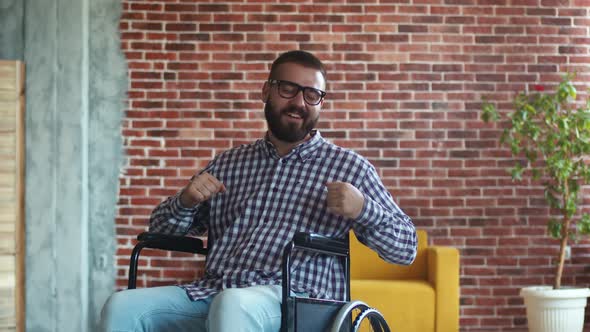 Happy Cheerful Bearded Disabled Man with Glasses is Sitting in Wheelchair Dancing and Rejoicing