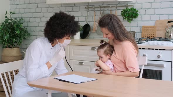 Afro American Woman Doctor Examines Little Girl at Home While Sitting at Table in Kitchen