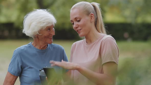 Female Trainer and Senior Woman Using Smartphone and Speaking Outdoors