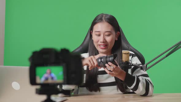 Asian Woman With Computer Reviewing Camera Len While Shooting Video By Camera On Green Screen