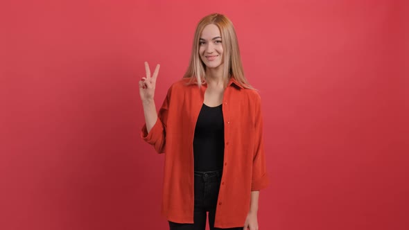 Smiling Young Woman Showing Peace Sign Over Red Background.