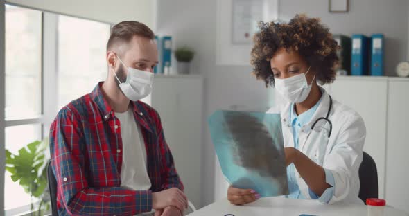 African Woman Doctor in Safety Mask Showing Xray to Patient at Medical Office in Hospital