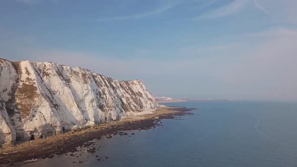 Drone flies low away from the White Cliffs of Dover with beautiful turquoise sea in the foreground.