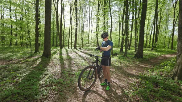 A Happy Cyclist is Standing in the Middle of the Forest and Looking at the Training Data on His