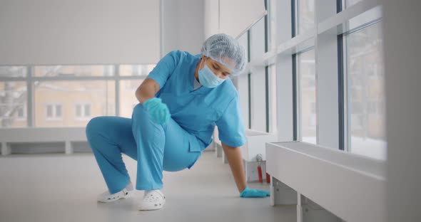 Sad Young Female Doctor Wearing Face Protective Mask Sitting on Floor at Hospital