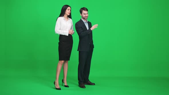 Young Man and Woman in Suits Stands in the Green Space of the Chromakey They Discuss Subjects While