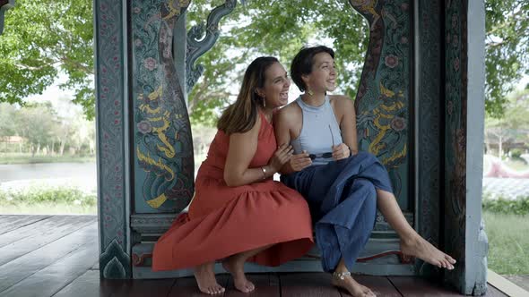 Two Female Adult Tourists Enjoying The Outdoor Views Sitting On A Carved Wooden Frame With Intricate