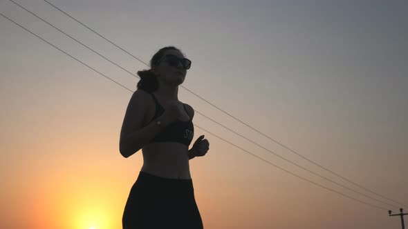 Active Slim Girl Jogging on Country Road with Evening Sky at Background. Female Sportsman Doing Run