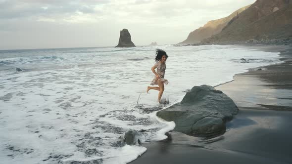 Young Woman in a Beautiful Dress Runs Along the Black Volcanic Black Sand Beach Benijo in the North