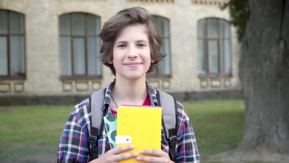 Portrait of Cute Intelligent Brunette Schoolboy Posing Outdoors. Happy Caucasian Boy with Books