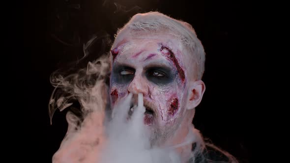 Zombie Man with Makeup with Wounds Scars and White Contact Lenses Blows Smoke From Nose and Mouth