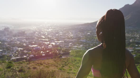 African american woman wearing wireless earphones stretching her arms outdoors