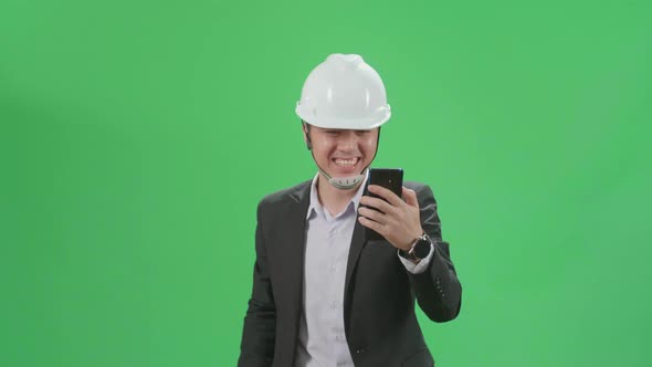 Asian Chief Engineer In The Hard Hat Having Video Call On Mobile Phone While Walking On Green Screen