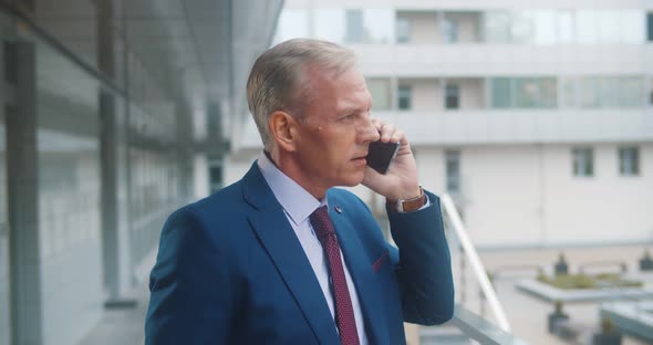 Successful Mature Businessman Talking on Mobile Phone Outside Business Center