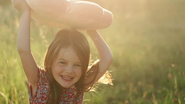 Little Cute Girl with Flowing Hair in a Summer Dress Sitting on the Grass and Playing with a Pink