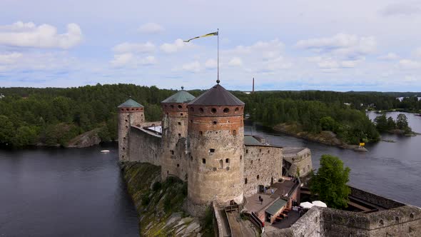 Drone pulling away from a medieval tower revealing a historical castle Olavinlinna on a beautiful su