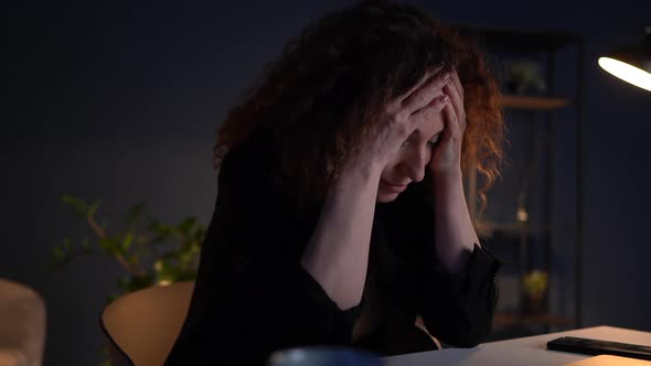 Close Portrait of a Frustrated Woman Holding Her Face with Her Hands While Sitting at Her Desk in