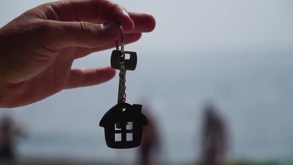 Keys with a Houseshaped Keychain in a Man's Hand on Sea Beach Background