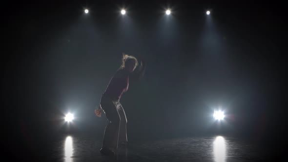 Strong Woman Practicing Capoeira in Darkness Against Spotlight in Studio.