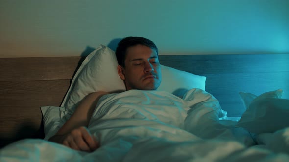 Young Man Lying on Pillow Under Blanket and Sleeping on Bed