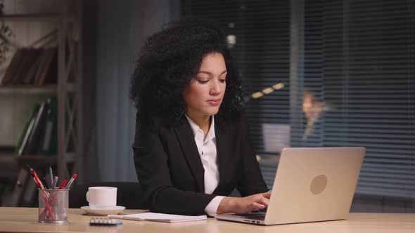 Portrait of African American Woman Texting with Client Using Laptop and Rejoices at Good Deal