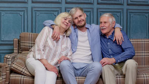 Family of Senior Grandparents with Adult Son Embracing Having Fun Looking at Camera Bonding at Home