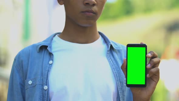 Serious black male teenager pointing finger into smartphone