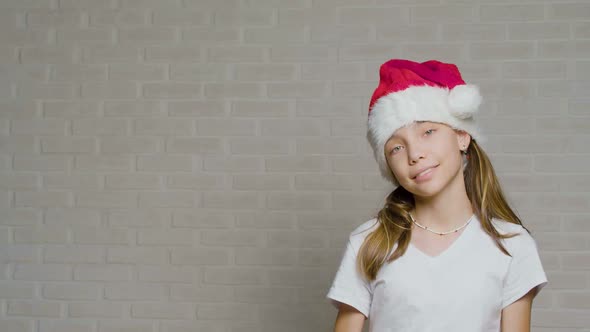 Teenager Girl in Santa Hat Holds a Christmas Gift in Her Hands Against a White Wall