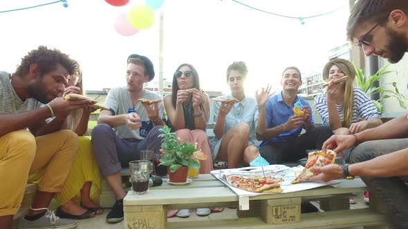 Young people sitting around the table and eating pizza on the rooftop terrace